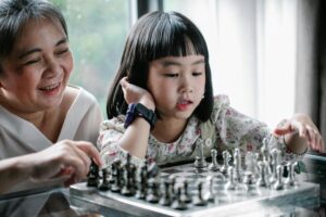 A grandmother and granddaughter bond while playing chess indoors, enjoying quality time together.